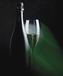 Bottle and glass of sparkling wine in green light