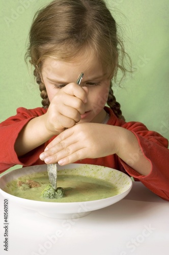Photo: Girl cutting a broccoli floret in vegetable soup Girl cutting a broccoli floret in vegetable soup