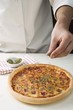 Sprinkling American-style ham pizza with oregano