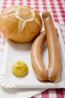 Frankfurters with mustard and bread roll on paper plate