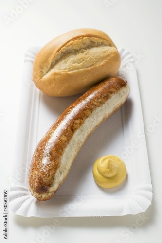 Photo: Sausage with mustard and baguette roll on paper plate Sausage with mustard and baguette roll on paper plate