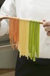 Home-made ribbon pasta hanging over wooden spoon
