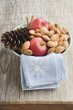 Red apples, almonds and cone in bowl on wooden table