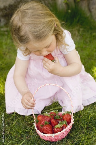 Photo: Small girl eating strawberries on grass Small girl eating strawberries on grass
