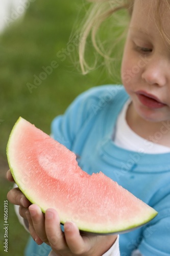 Photo: Small girl holding a slice of watermelon with a bite taken Small girl holding a slice of watermelon with a bite taken