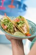 Foto: Woman holding plate of two chicken tacos Woman holding plate of two chicken tacos