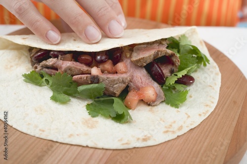 Photo: Hand folding tortilla over beef filling Hand folding tortilla over beef filling