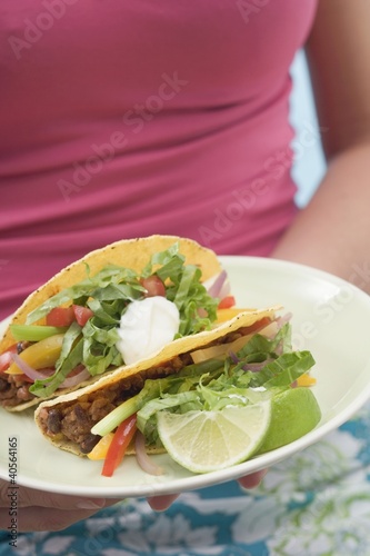 Foto: Woman holding plate with two tacos Woman holding plate with two tacos