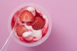 Strawberry yoghurt in plastic pot with spoon (overhead view)