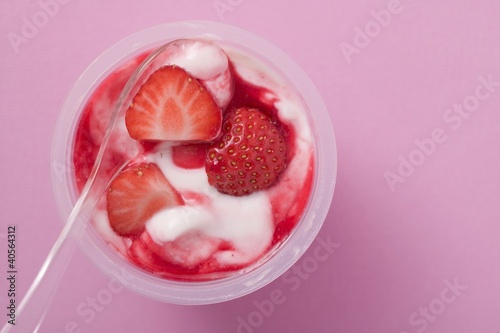 Photo: Strawberry yoghurt in plastic pot with spoon (overhead view) Strawberry yoghurt in plastic pot with spoon (overhead view)