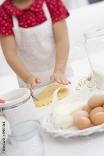 Foto: Small girl flattening dough with her hands Small girl flattening dough with her hands