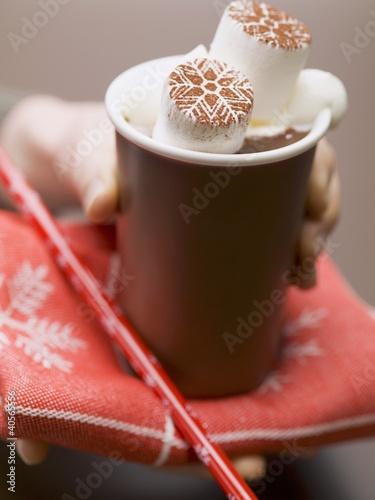 Photo: Hand holding beaker of hot chocolate with marshmallows & cream Hand holding beaker of hot chocolate with marshmallows & cream