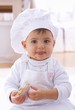 Foto: Little girl in chef's hat eating biscuit Little girl in chef's hat eating biscuit