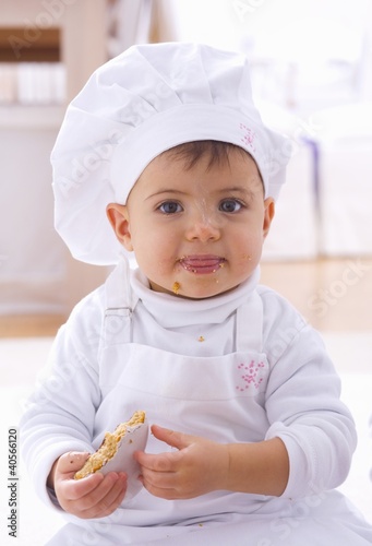 Photo: Little girl in chef's hat eating biscuit Little girl in chef's hat eating biscuit