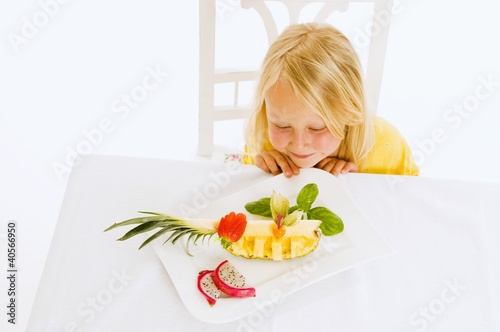 Photo: Girl sitting at table in front of plate of fruit Girl sitting at table in front of plate of fruit