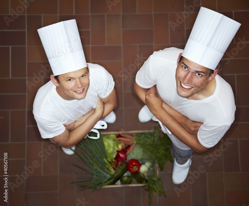 Photo: Two chefs with their arms folded beside crate of vegetables Two chefs with their arms folded beside crate of vegetables