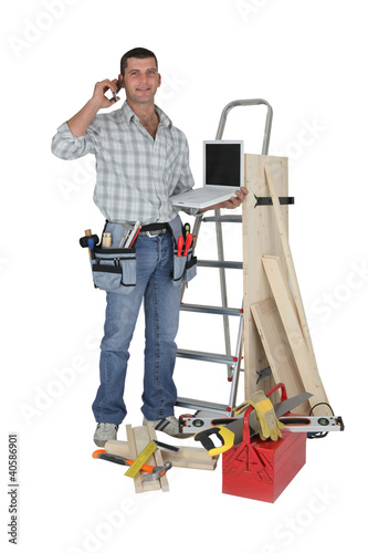 Foto: Carpenter stood with equipment making telephoning customer Carpenter stood with equipment making telephoning customer