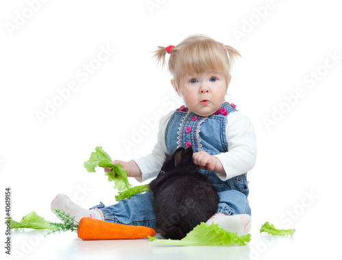 Photo: Funny little girl feeding a rabbit with carrot and lettuce on th Funny little girl feeding a rabbit with carrot and lettuce on th