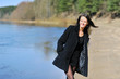 Girl in a dark coat walking along the river laughing