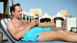 Young man sending sms while sunbathing by the pool