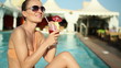 Woman sitting by swimming pool and drinking exotic cocktail