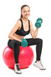 Female lifting up a dumbbells seated on a fitness ball