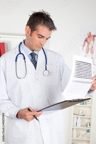 Photo: Male Doctor Looking at Clipboard Male Doctor Looking at Clipboard