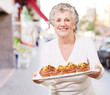 portrait of senior woman showing a chocolate muffin tray at stre portrait of senior woman showing a chocolate muffin tray at stre