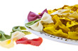 Uncooked rainbow farfalle pasta spilling from plate on white bac Uncooked rainbow farfalle pasta spilling from plate on white bac