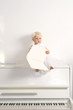 A girl in white dress sitting on a piano in the room A girl in white dress sitting on a piano in the room