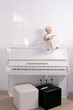 A girl in white dress sitting on a piano in the room A girl in white dress sitting on a piano in the room