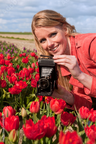 Photo: Dutch blond girl with old photo camera in field with tulips Dutch blond girl with old photo camera in field with tulips