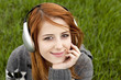 Young fashion girl with headphones sitting at green spring grass