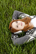 Young fashion girl with headphones lying at green spring grass.