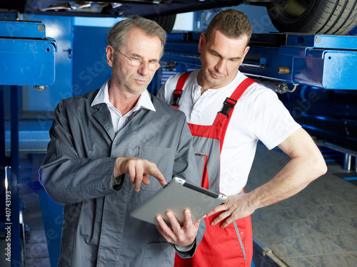 Foto: Master mechanics inspecting the engine of a car with touchpad Master mechanics inspecting the engine of a car with touchpad