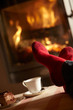 Close Up Of Mans Feet Relaxing By Cosy Log Fire With Tea And Cak