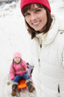 Mother Pulling Daughter On Sledge On Snowy Street In Ski Resort