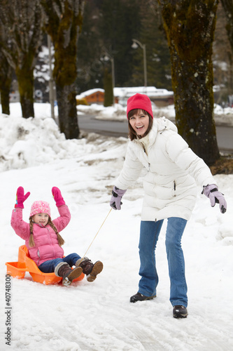 Photo: Mother Pulling Daughter On Sledge Along Snowy Street In Ski Reso Mother Pulling Daughter On Sledge Along Snowy Street In Ski Reso