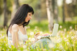 Cute woman with white laptop in the park with dandelions