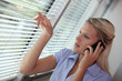 Businesswoman peering through blinds during call