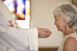 Older woman taking communion from priest