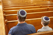 Father and son in yarmulkes sitting in synagogue