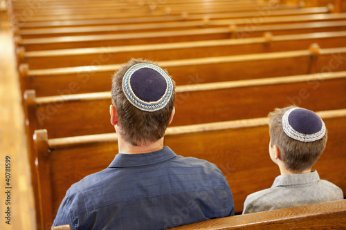 Photo: Father and son in yarmulkes sitting in synagogue Father and son in yarmulkes sitting in synagogue