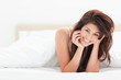Photo: Woman is lying at the end of the bed under the quilt while smili Woman is lying at the end of the bed under the quilt while smili