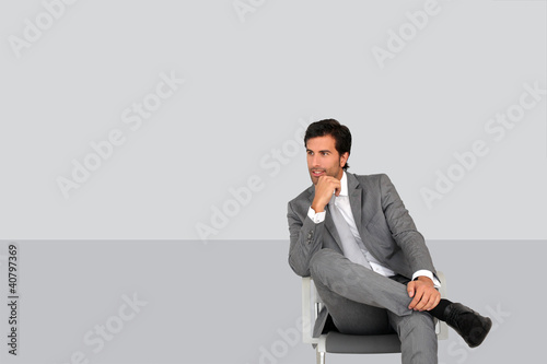 Photo: Businessman sitting on chair on grey background Businessman sitting on chair on grey background
