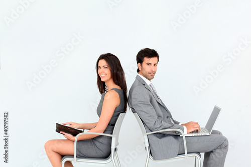 Photo: Business people sitting in chairs back to back Business people sitting in chairs back to back