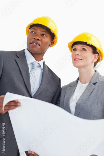 Photo: Smiling business people wearing hard hats are holding a paper Smiling business people wearing hard hats are holding a paper