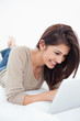 Foto: Woman smiling as she uses her tablet while lying on the bed Woman smiling as she uses her tablet while lying on the bed