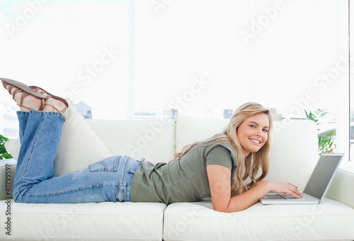 Foto: Woman smiling as she looks forward, legs raised and using her la Woman smiling as she looks forward, legs raised and using her la