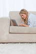 A smiling woman is lying on a couch using a tablet